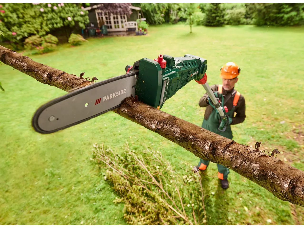 Homem usa uma serra de poda a bateria PARKSIDE para aparar um galho no jardim.