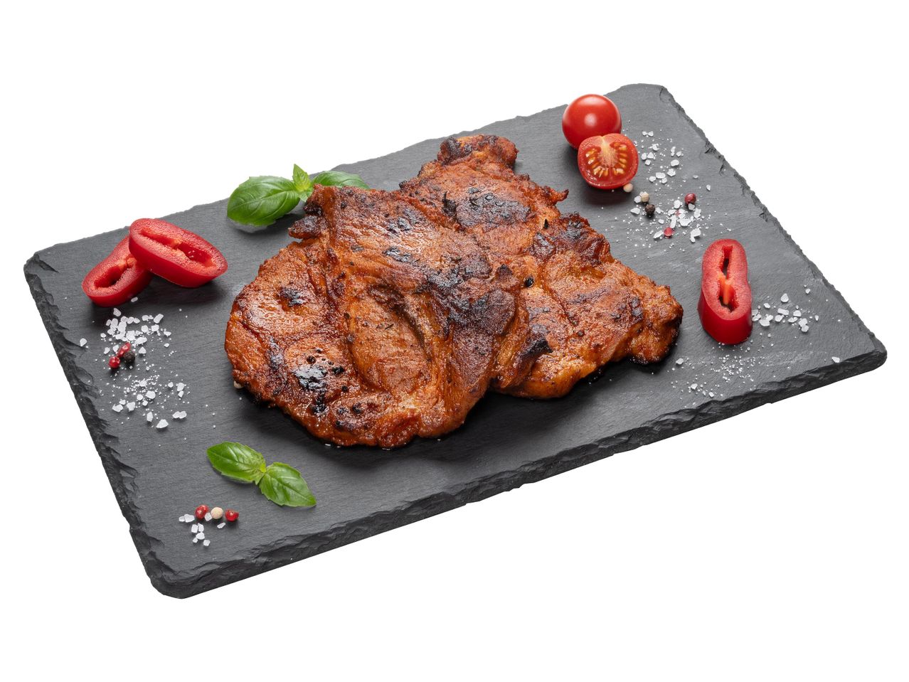 Grillezett hús paradicsommal, bazsalikommal és fűszerekkel egy fekete palatáblán.