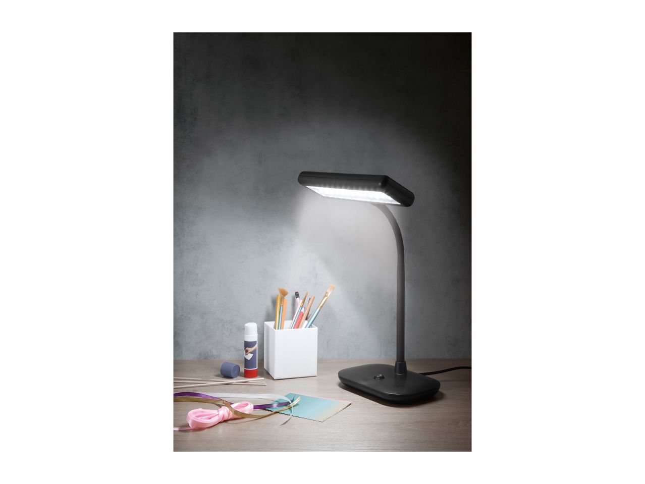 Desk lamp illuminating a craft area with brushes, glue, and ribbons.