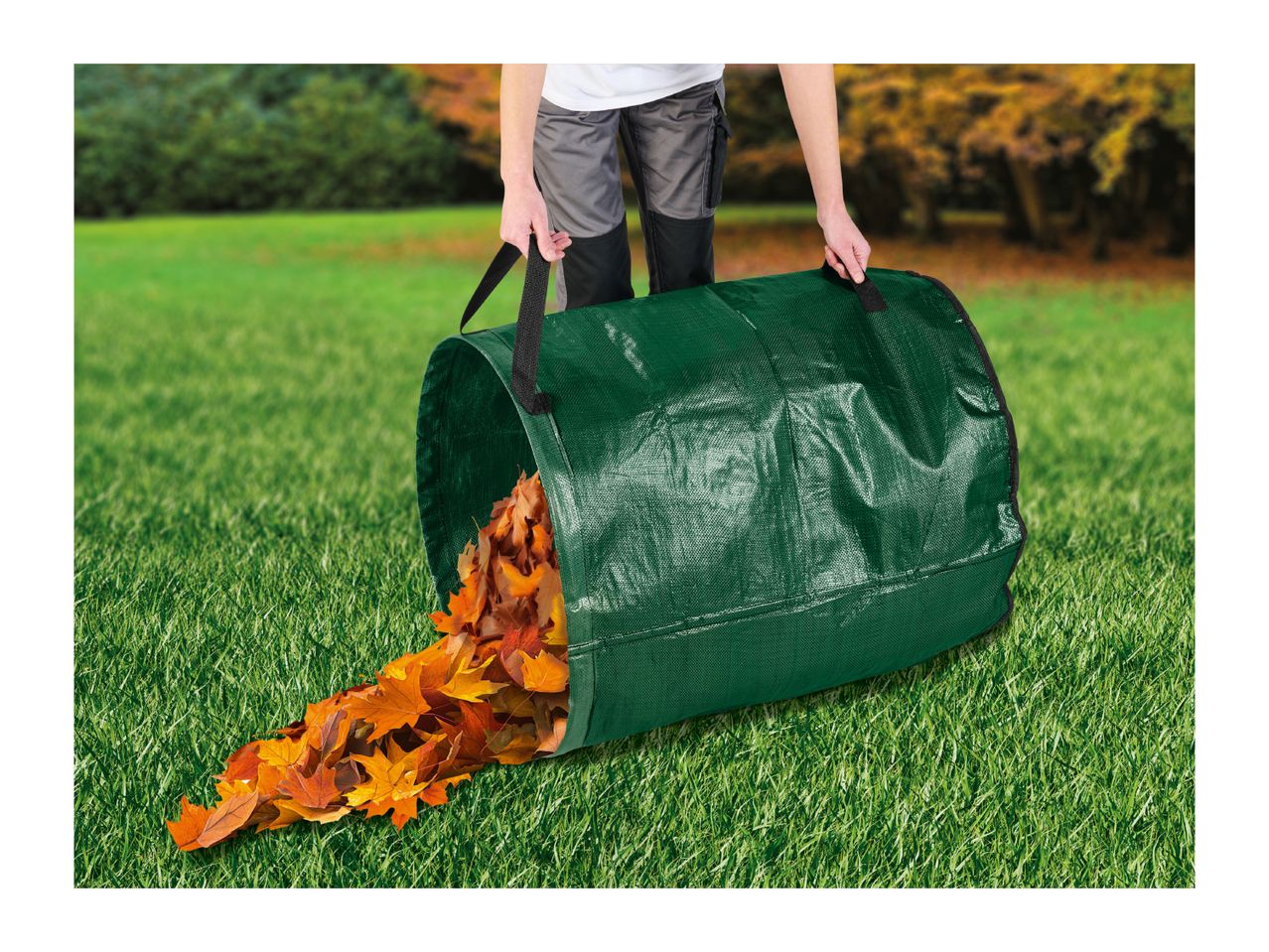 Person emptying a green garden waste bag filled with autumn leaves onto a green lawn.