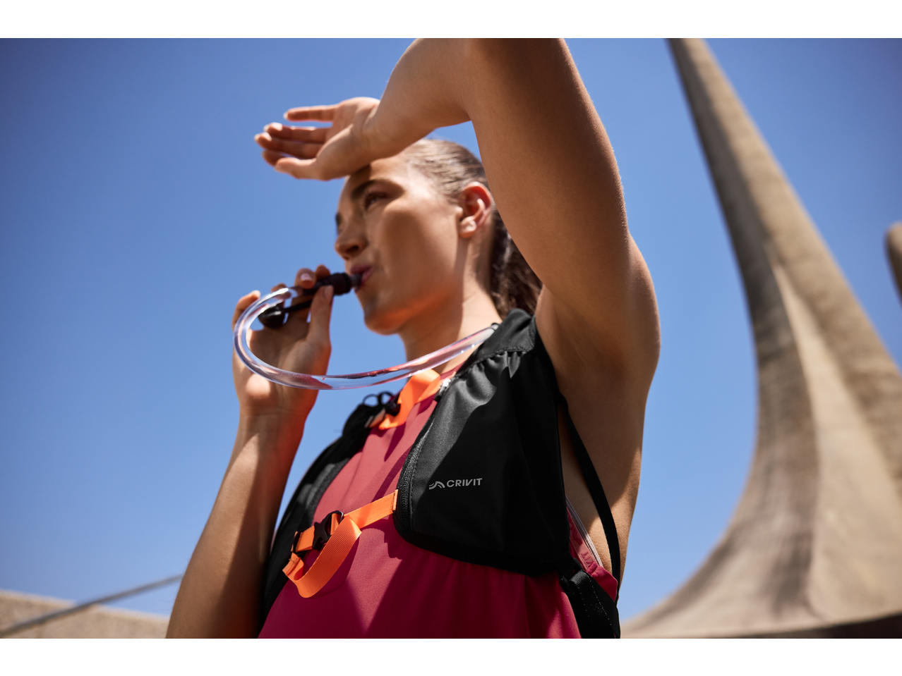 Woman drinking from a hydration pack, shielding her eyes from the sun.