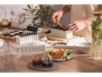 Kit de fazer sushi Silvercrest em uso, com uma pessoa a adicionar ingredientes a um rolo de sushi.