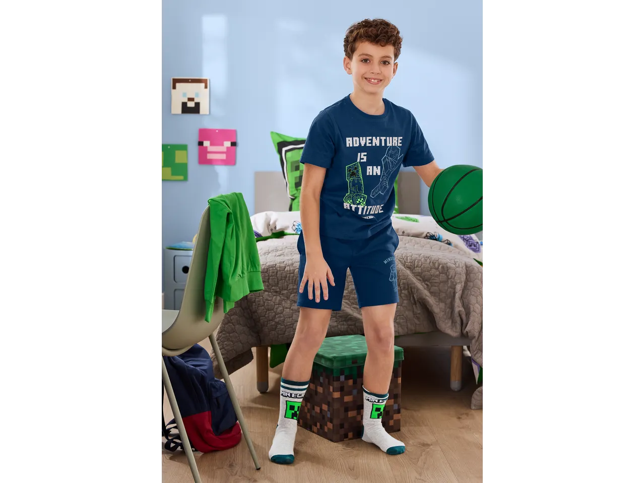 Boy in a blue Minecraft T-shirt and shorts, holding a green basketball in a Minecraft-themed room.