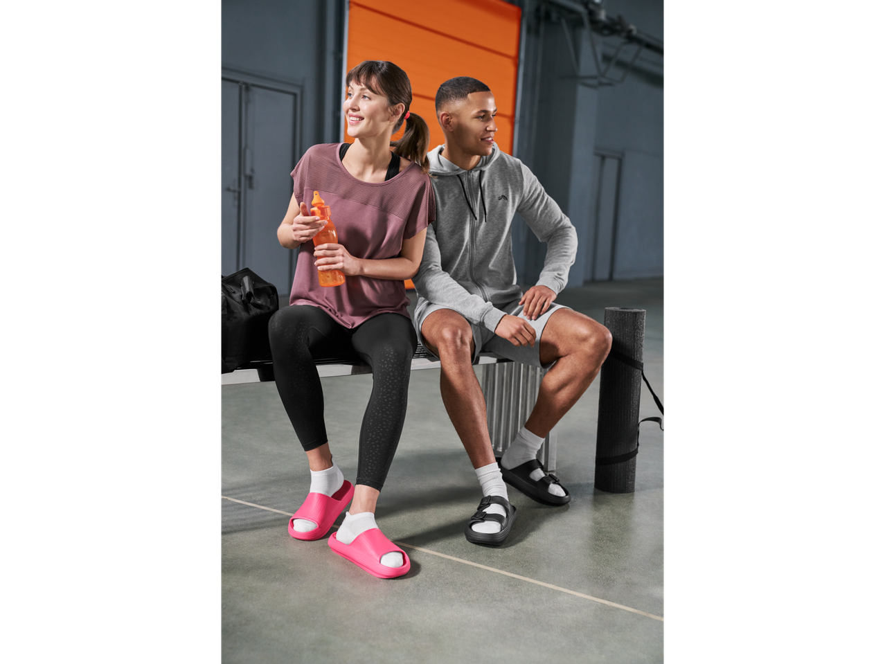 Mulher com camisola funcional CRIVIT e homem com hoodie CRIVIT sentados num banco.