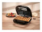 Waffle maker with two golden waffles, a plate of waffles with berries, and whipped cream.