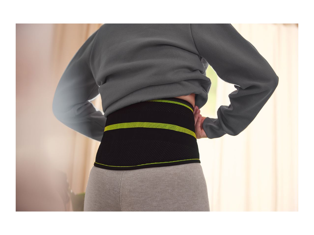 Person wearing a black and neon green back support belt over gray leggings.