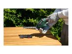 Person in gloves holding a hedge trimmer with another attachment on a wooden table.