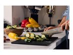Person slicing zucchini on a cutting board with other fresh vegetables nearby.