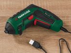 A Parkside PAS 4 D7 cordless screwdriver with USB charging cable lies on a wood surface.