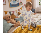 Baby wearing Lupilu baby shoes, standing on a yellow mat in a nursery.