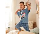 A toddler in Paw Patrol pajamas plays on a bed.