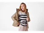 Donna con giacca leggera beige e maglione a righe.