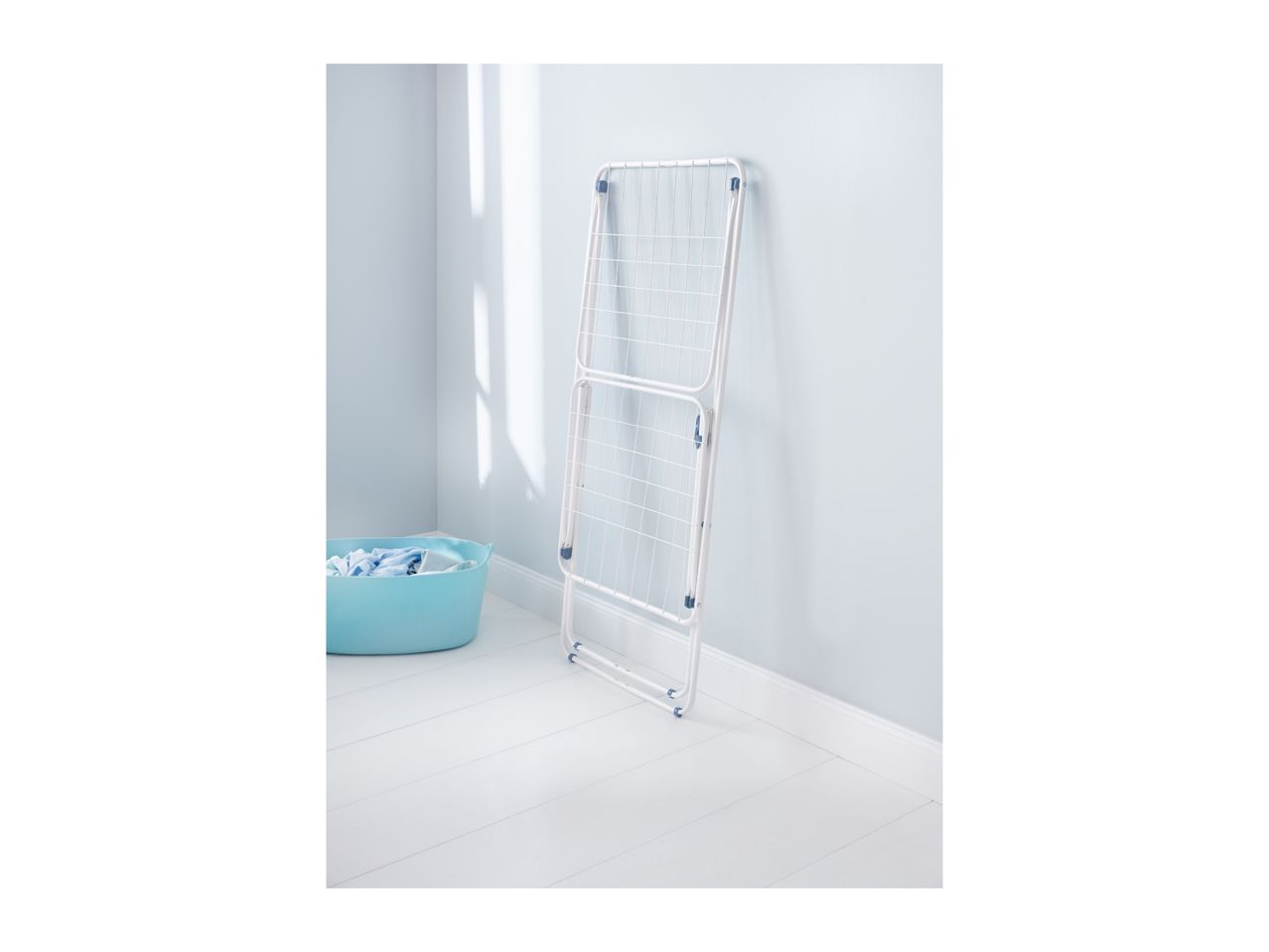 A white foldable laundry drying rack stands against a light blue wall, next to a light blue laundry basket.