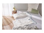 Two vacuum storage bags with textiles on a bed, with a rug and side table nearby.