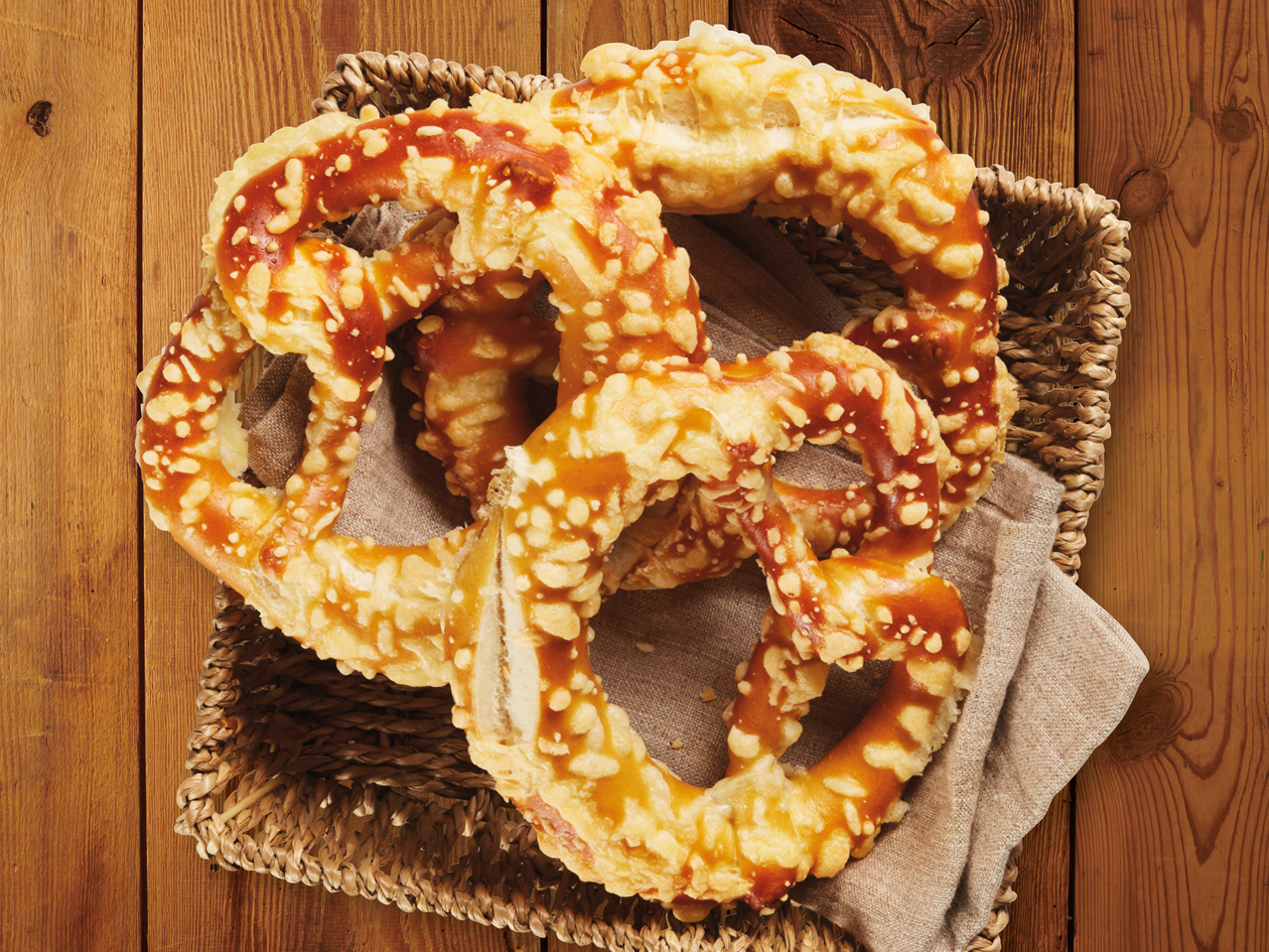 Кошничка с три солени брецела, поръсени със сирене, върху дървена маса.