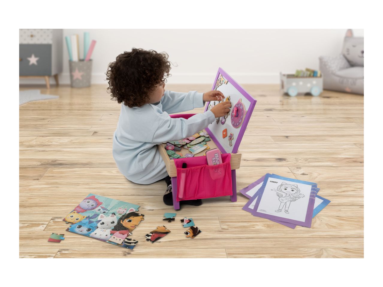 A child playing with a wooden easel, magnetic letters, and a puzzle on a wooden floor.