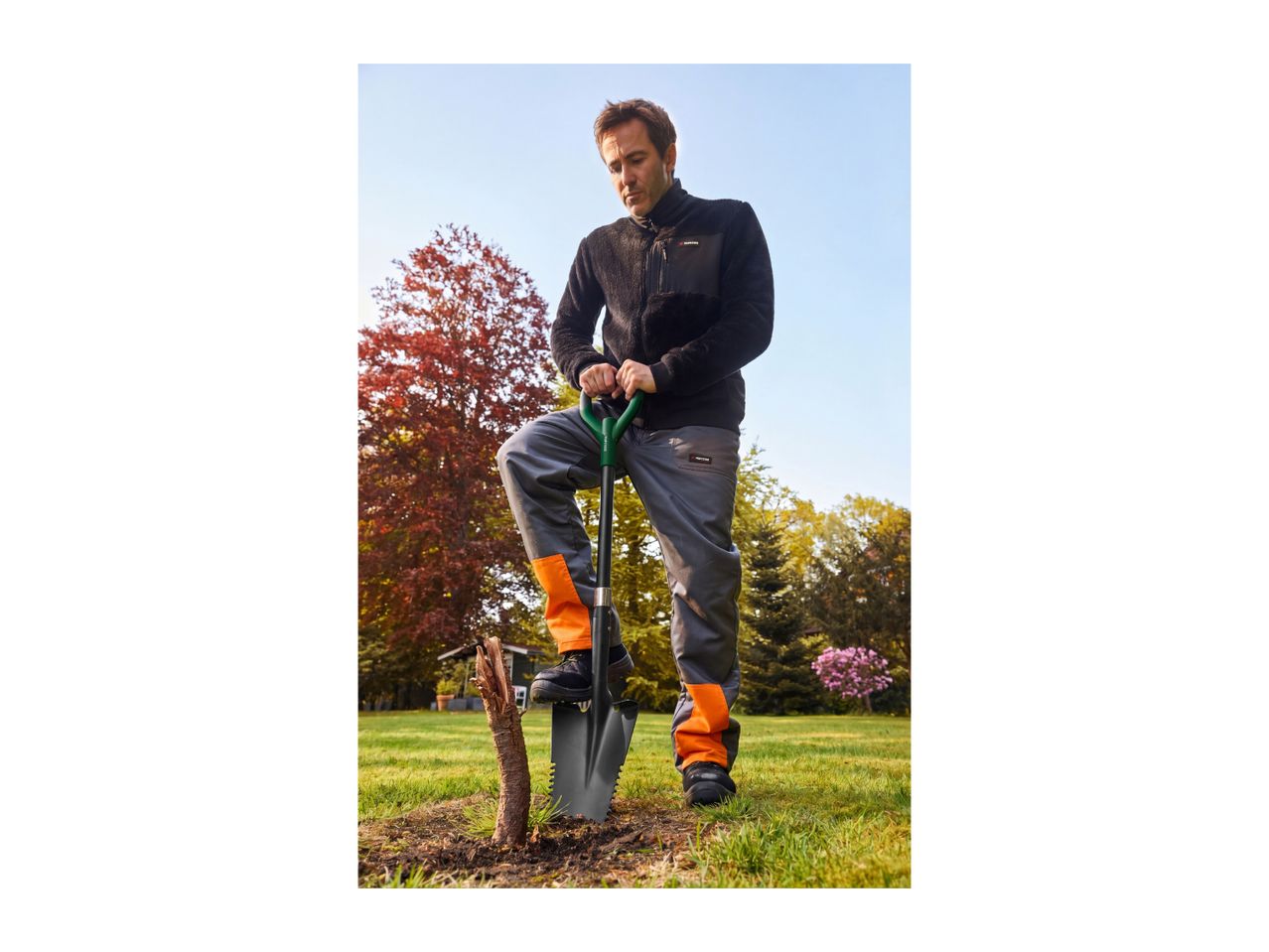 Man in workwear using a shovel to dig in a garden.