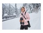 A woman in a pink winter jacket holding binoculars in a snowy landscape.