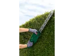 Persona che taglia una siepe con un tagliasiepi verde.