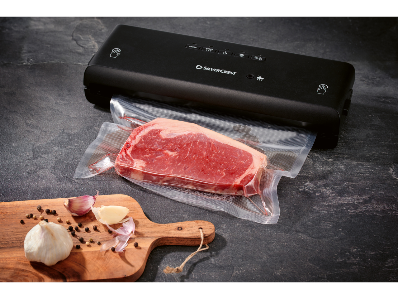 Máquina de vácuo SilverCrest com carne embalada a vácuo e alho numa tábua.