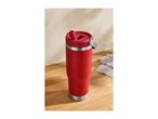 Red insulated tumbler with a straw lid on a wooden surface next to a grey cloth.
