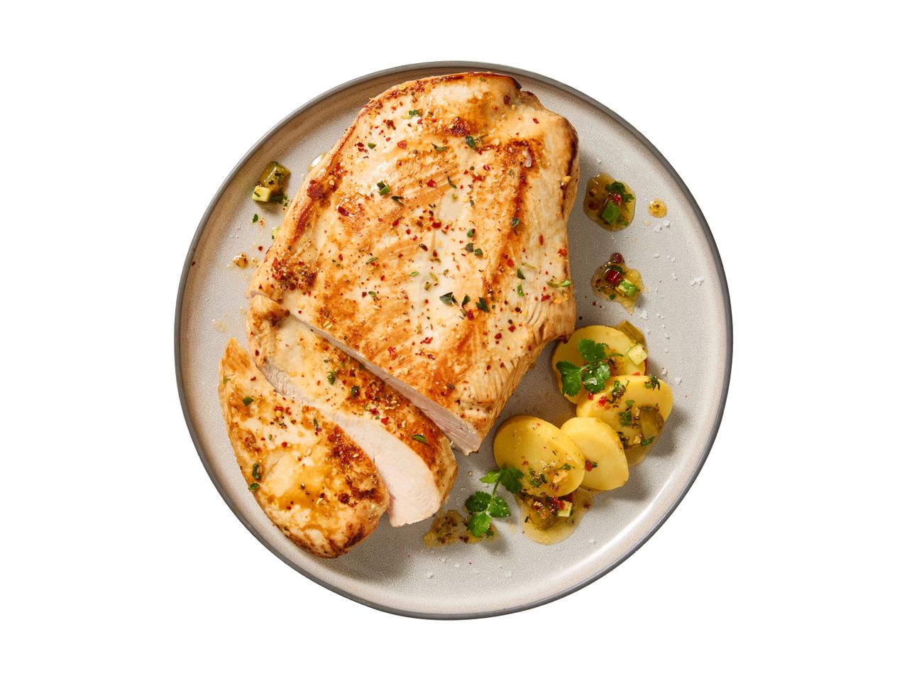 Grilled chicken breast with sliced potatoes and a fresh herb dressing on a plate.