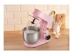 Pink stand mixer with whisked cream in a stainless steel bowl on a wooden counter with eggs and kitchenware.