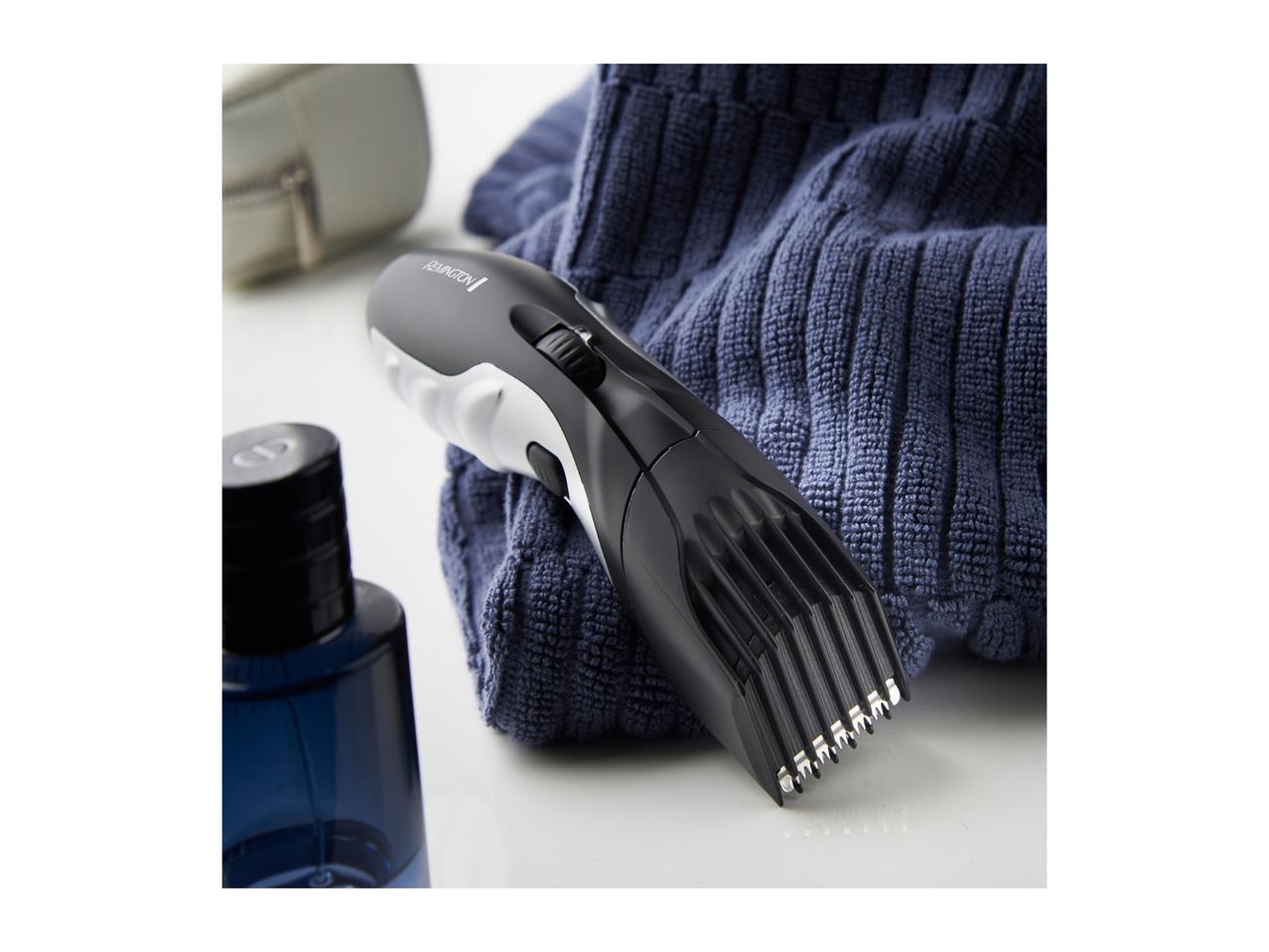 Remington hair clipper on a blue towel next to a bottle of cologne.