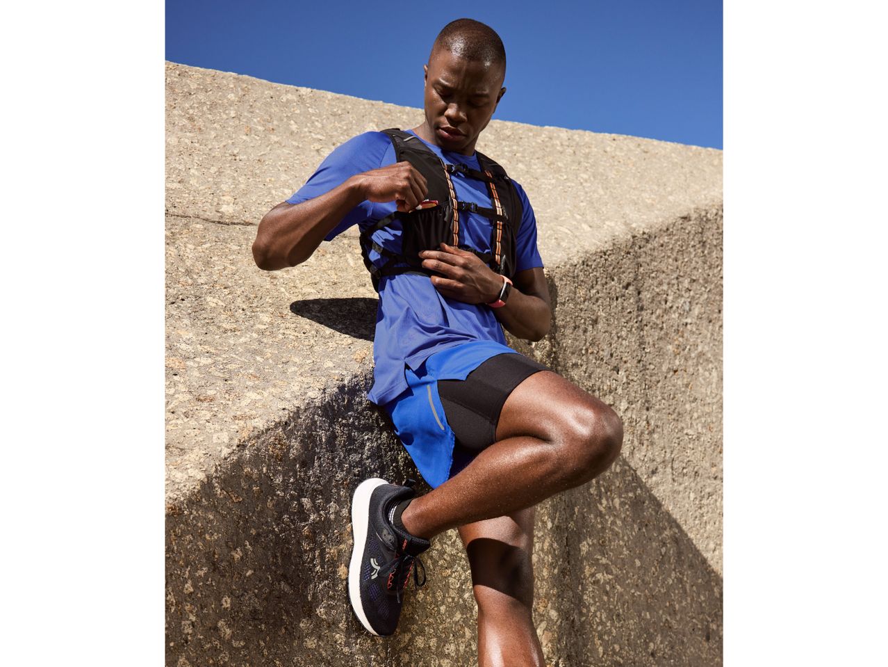 Man in blue athletic wear and hydration vest, taking an energy gel break during a run.