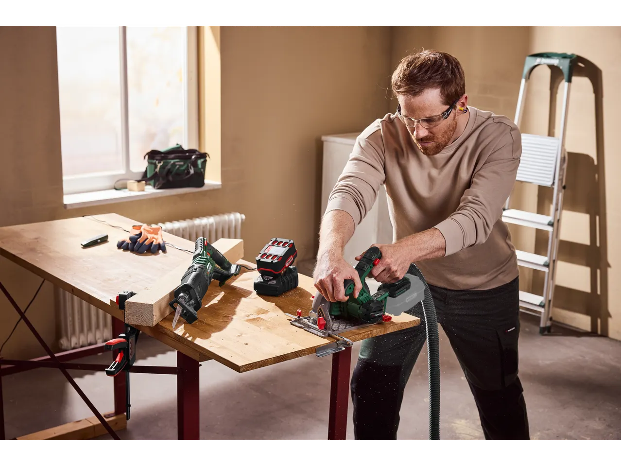 Homem a usar uma serra circular sem fios Parkside® para cortar madeira numa bancada de trabalho.