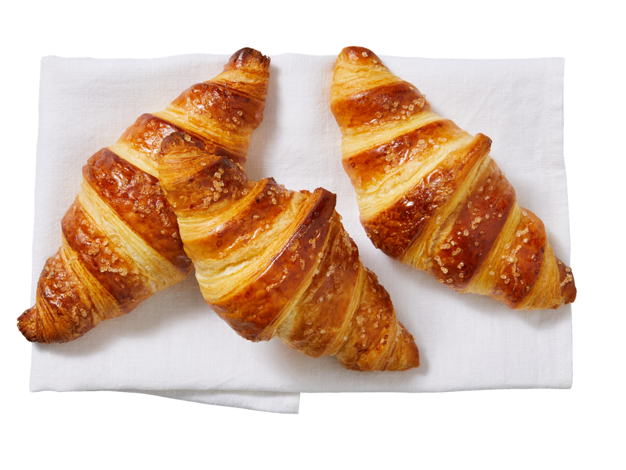 Trys auksiniai XXL kruasanai, pabarstyti cukrumi, ant baltos servetėlės.