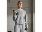 Woman in a gray hoodie and sweatpants holding dumbbells