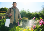 Man using a Parkside® Garden Pressure Sprayer on plants in a sunny garden.