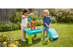 Two children playing with a water and sand table, bubble machine, and toy suitcase in a garden.