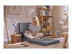 Woman sitting on a grey foldable mattress, writing in a notebook, in a cozy living room.