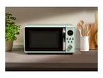 A mint green SilverCrest microwave on a kitchen counter with a plant and utensils.