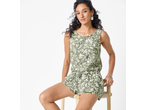 Mulher com macacão verde com padrão floral branco, sentada num banco.
