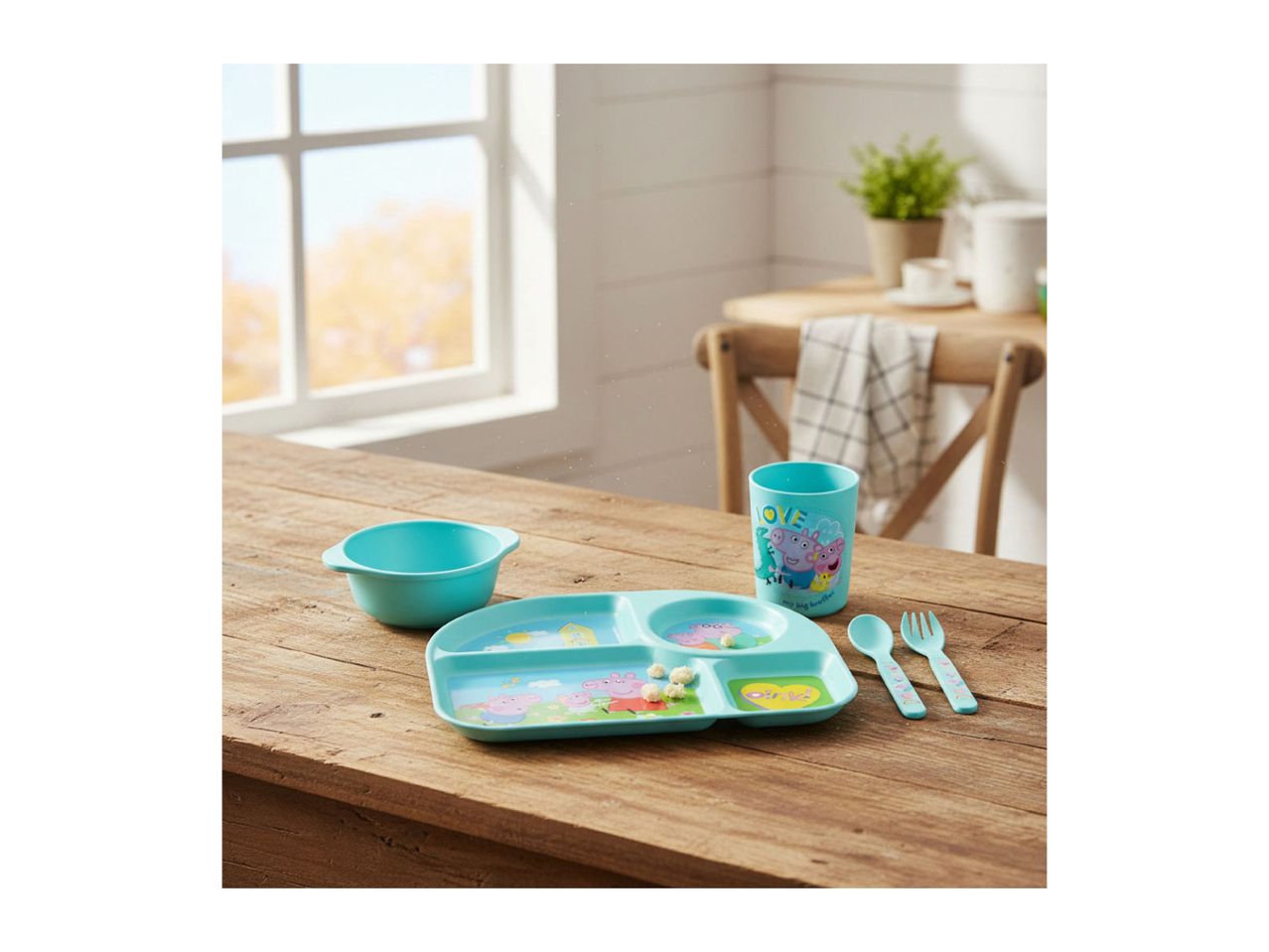 Children's dining set with a divided plate, bowl, cup, spoon, and fork on a wooden table.