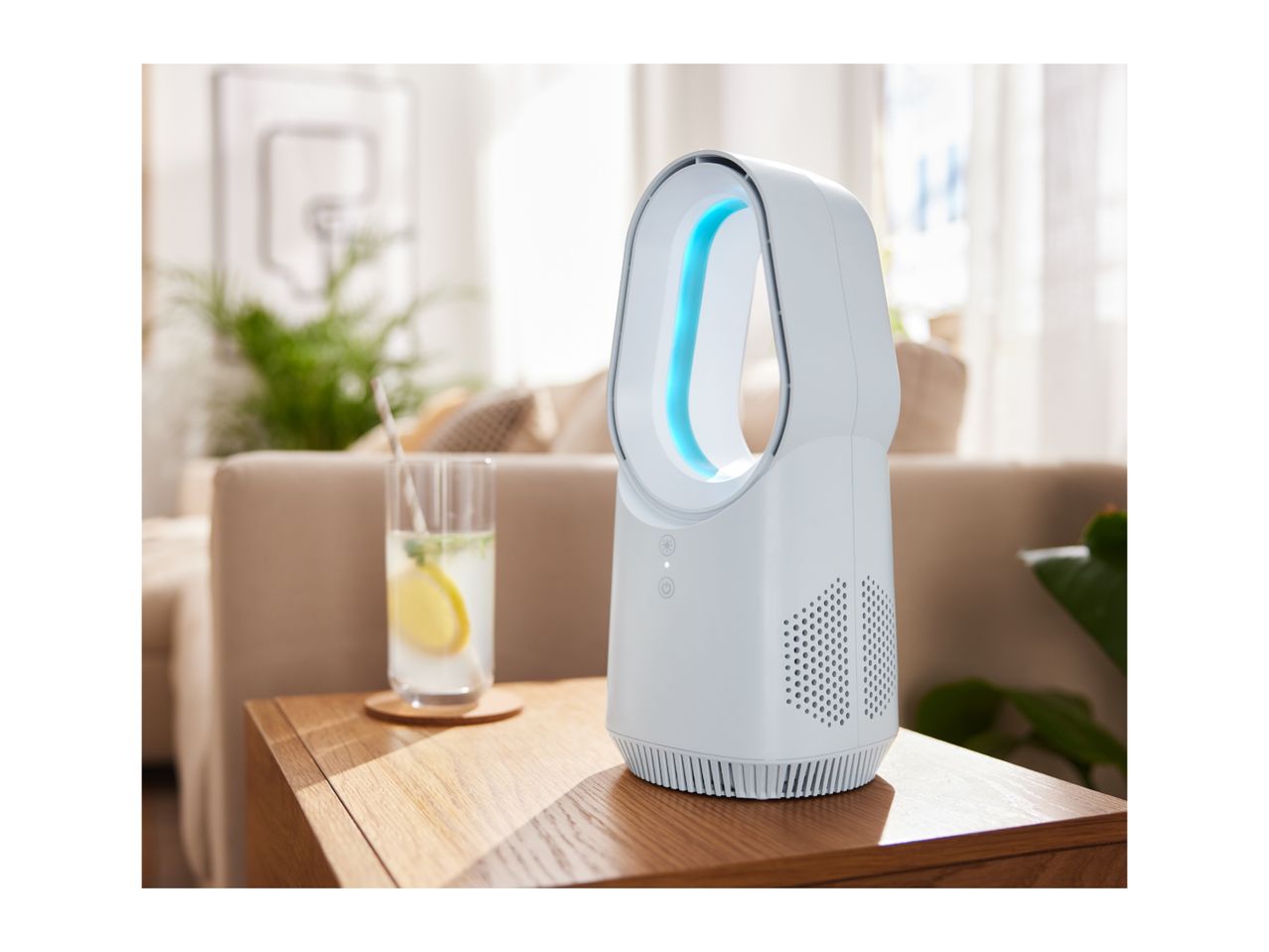 White air purifier with blue light on a wooden table next to a glass of lemonade in a living room.