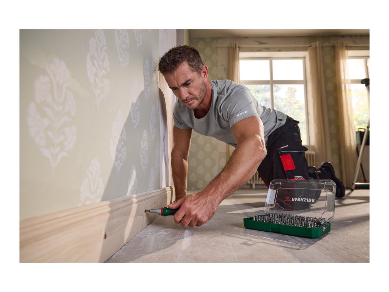 Man installing skirting board with a screwdriver and a bit set on the floor.