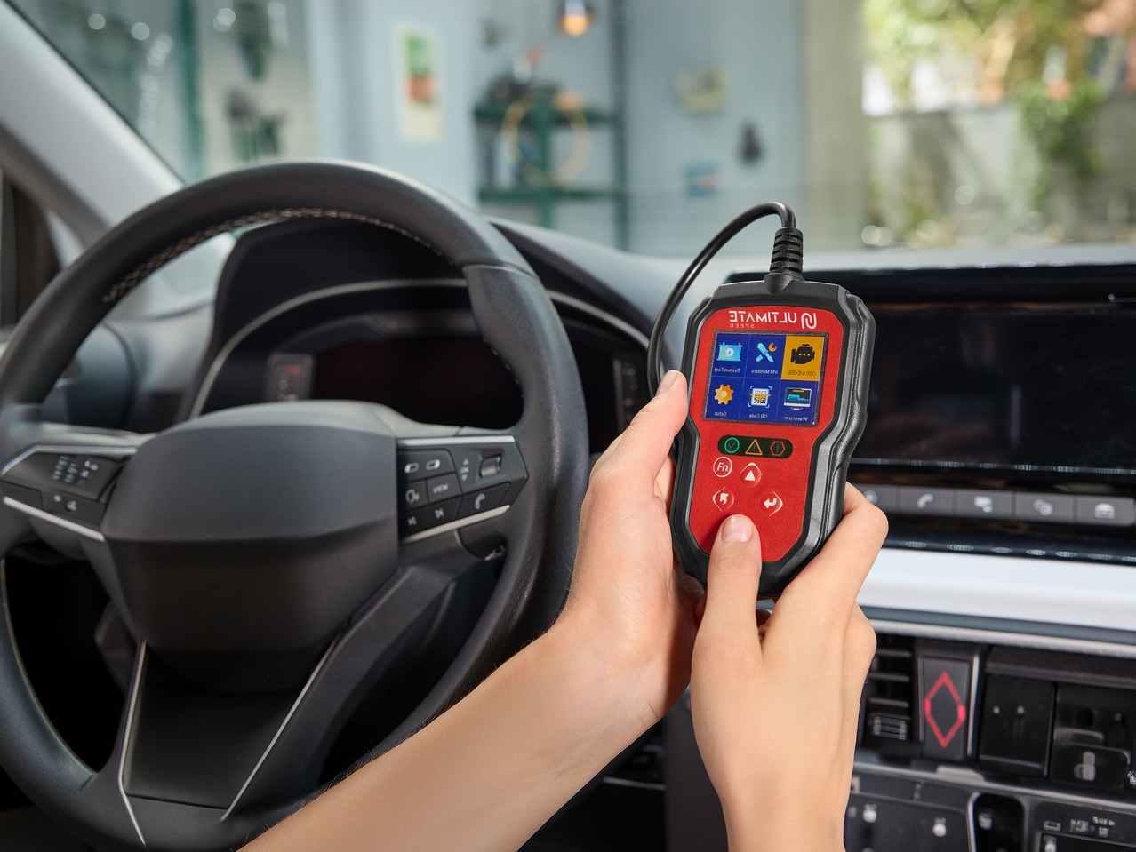 Χέρια κρατούν ένα διαγνωστικό εργαλείο αυτοκινήτου με οθόνη που εμφανίζει εικονίδια, μέσα σε ένα αυτοκίνητο.