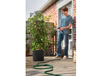 A man waters a Parkside® Tomato Planter with a hose on a sunny balcony.