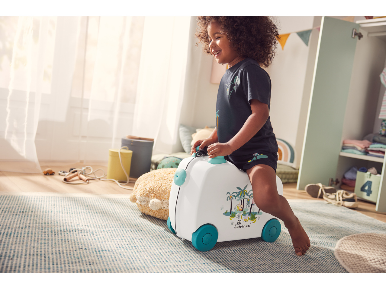 Smiling child riding a white suitcase with jungle animals and '60 bananas!' text.