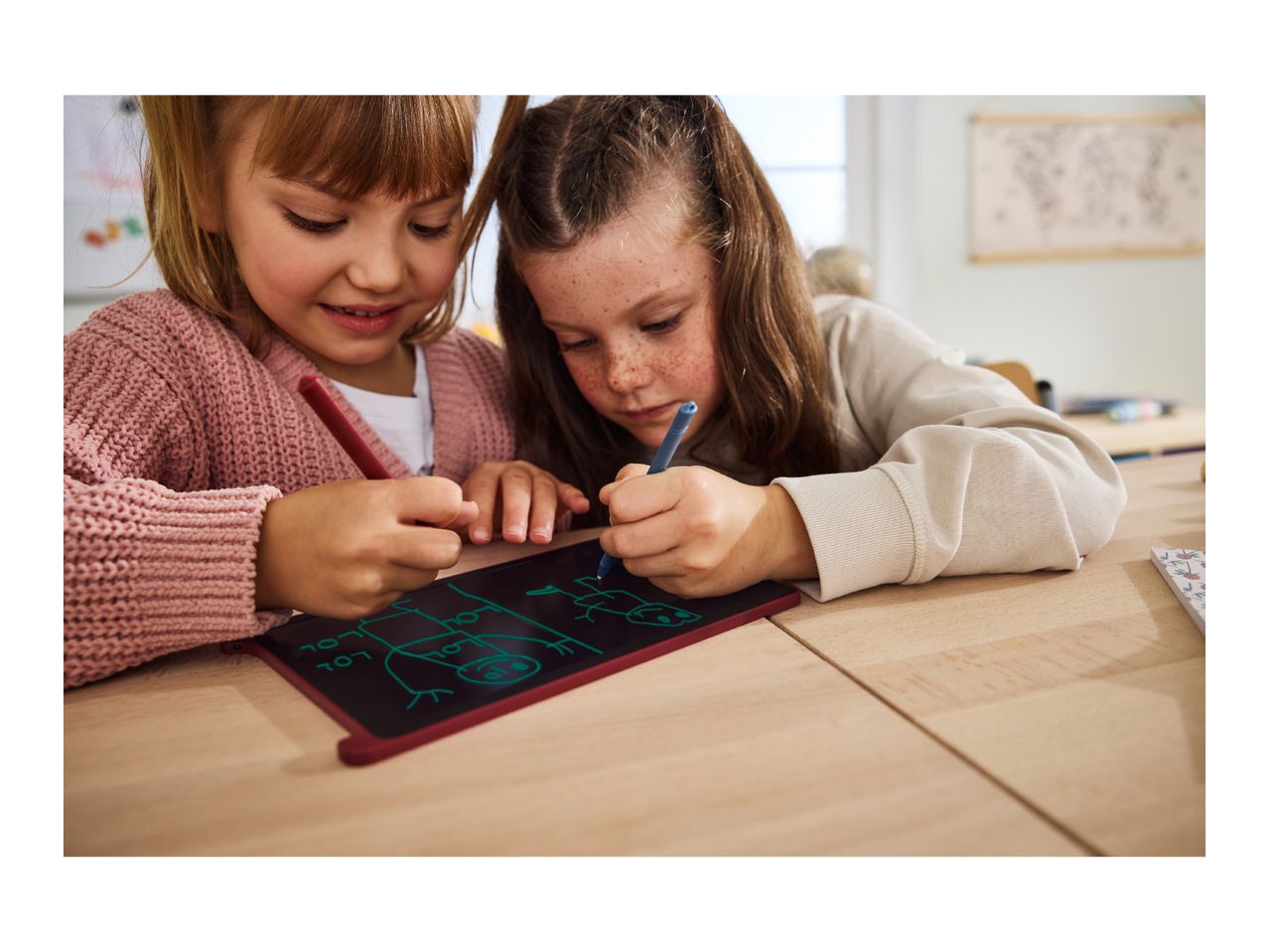 Two girls drawing on a digital writing tablet with styluses, creating stick figures and text.