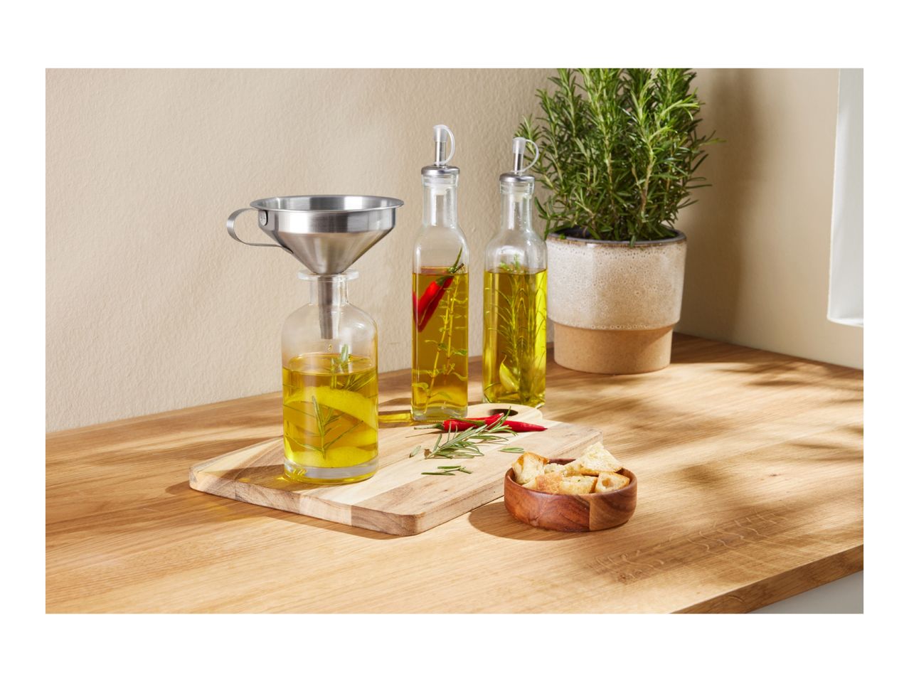 Infused olive oil bottles with herbs, chili, and lemon, with a funnel and croutons.