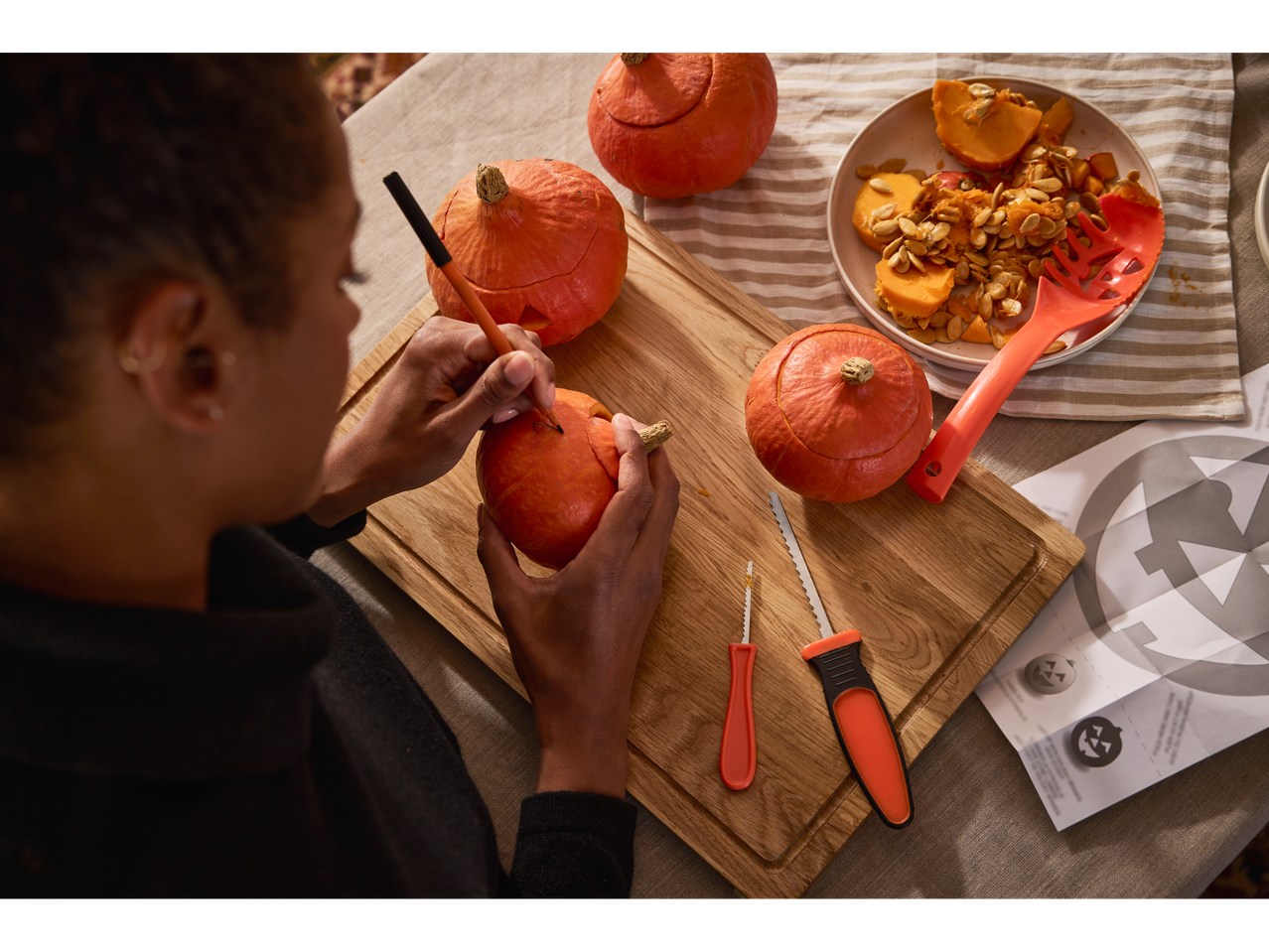 A person carving a pumpkin with a LIVARNO home Halloween Pumpkin Carving Set.