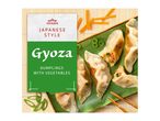 Japanese style gyoza dumplings with vegetables on a green plate with chopsticks.