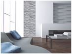 Un salon moderne avec un canapé gris, des coussins bleus, un mur en pierre et une table basse en verre.