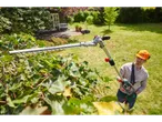 A man uses a long-reach Laserline hedge trimmer to prune a bush in his garden.