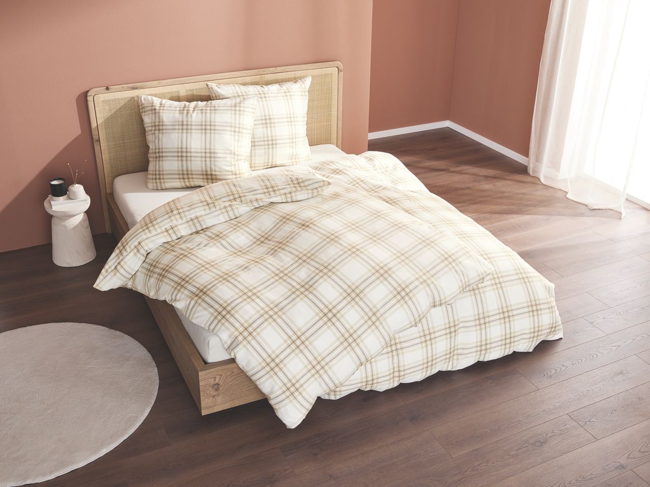 Bedroom with wooden bed, plaid duvet cover, and white side table.